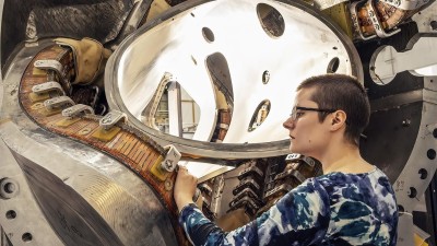 Graduate student Alexandra LeViness stands next to part of a stellarator, a twisty fusion device designed to confine ultra-hot plasma to facilitate fusion reactions.